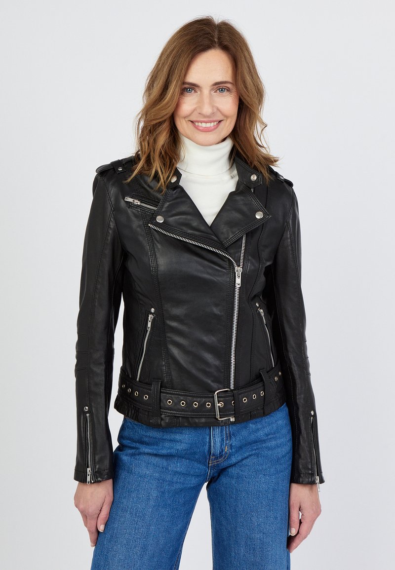 Zwarte leren motorjack met zilveren onderdelen, asymmetrische rits en een ceintuur in de taille. Gestyled met een witte coltrui en blauwe jeans.