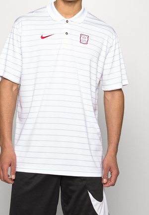 Homme portant un polo blanc rayé avec un logo Nike rouge et un emblème des Miami Marlins, associé à un short Nike noir et blanc.