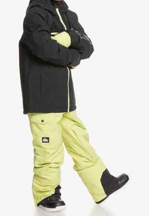 Veste noire isolée avec des accents jaunes fluo, associée à un pantalon de neige jaune vif arborant un logo. Des bottes d'hiver noires complètent le look.