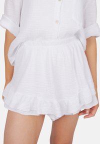 Shorts blancs texturés avec un ourlet volant et une taille élastique, en tissu léger et respirant, adaptés aux temps chauds.