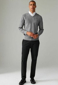 Pulover gri tricotat cu decolteu în V, manșete ribbate și un logo mic; asortat cu pantaloni negri și pantofi negri. Design simplu și curat.