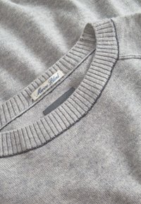 Grauer Merinowoll-Mix-Pullover mit geripptem Kragen, der eine subtile Textur aufweist und ein blaues Etikett mit der Aufschrift "Merinowolle-Mix" trägt.
