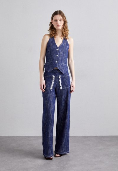 Denim to-delt sett i mørk blå. Ermeløs, tettsittende vest med knapper, sammen med bredbein bukser med revne lommer og kontraststing.