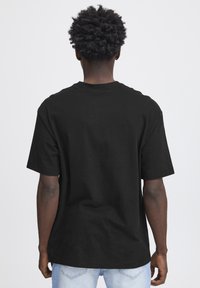 Tricou scurt negru din bumbac, cu guler rotund, croi lejer și design simplu pe spate. Purtați-l cu blugi albastre deschise.