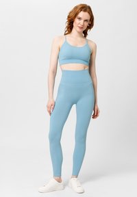 Světle modrý sportovní set, který zahrnuje zkrácený top na tenkých ramínkách a legíny s vysokým pasem ve žebrované textuře. Bílé tenisky.