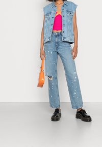 Denimväst, rosa kort topp, slitna ljusblå jeans med vita färgfläckar, orange handväska och svarta platåsandaler.