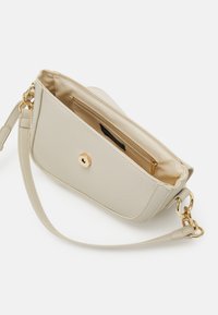 Beige tekstureret skuldertaske med guldspænde og ringe, åben for at vise den glatte stofforing og den lynlåselukket indvendige lomme.