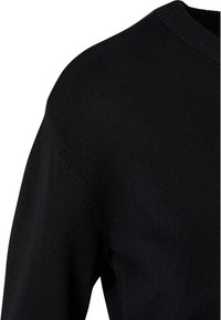 Gros plan sur un pull noir en maille montrant les détails de l'épaule, de la manche et du col rond côtelé.