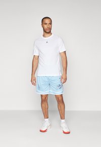 White t-shirt with a black logo, light blue mesh shorts with white trim and graphics, and white sneakers with red accents.