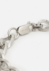 Silver metal chain bracelet featuring interlocking links, a polished finish, and a clasp engraved with "Calvin Klein."
