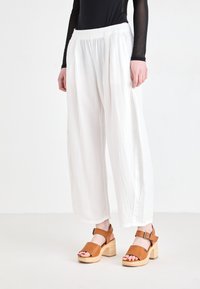 White, textured wide-leg pants with an elastic waistband paired with tan block-heeled sandals.  Focus on simple, relaxed design and materials.