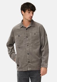 Ribjakke i grå med krave, to forlommer, sorte knapper og lange ærmer med knappede manchetter.