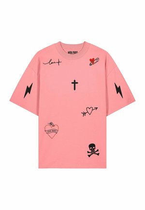 Giovane donna con lunghi capelli biondi che indossa una maglietta rosa larga con grafiche nere e jeans larghi azzurri, in piedi e che guarda indietro.