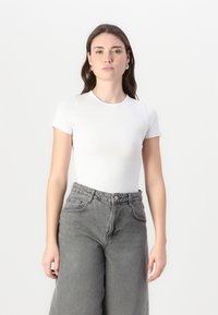 Bílá krátkosrstá tričko s krátkým rukávem spojené s vysoko pasovými, volně padnoucími šedými džíny. Jednoduchý design, měkká tkanina, s klasickým kulatým výstřihem.