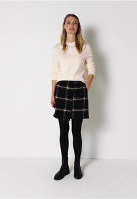 Vaaleanbeige neule, musta ruudullinen hame ja mustat sukkahousut. Hameessa on etupainike ja kaulusmuotoilu. Mustat nilkkurit täydentävät asun.