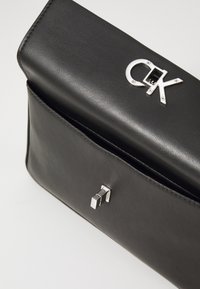 Borsa a mano in pelle nera con logo e chiusura in argento, con superficie texture e forma rettangolare elegante. Dettagli di cucitura sottili visibili.