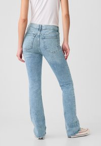 Lichtblauwe uitlopende spijkerbroek met een gestructureerde afwerking, voorzien van achterzakken en een hoge taille, gecombineerd met een aansluitend wit topje.