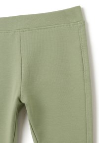 Plan rapproché de pantalons à taille élastique vert clair avec des coutures visibles et une texture de tissu lisse.