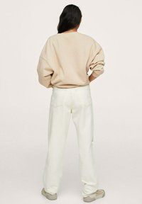 Beige Oversized-Sweatshirt und weiße weit geschnittene Jeans, kombiniert mit hellen Schuhen. Glatter Stoff, lockere Passform, minimalistisches Design.
