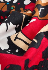 Farverigt stof med en sort baggrund, der har røde, hvide og brune mønstre. Materialet synes blødt med en glat tekstur.