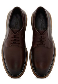 Scarpe in pelle marrone con una finitura liscia, dotate di punta arrotondata, chiusura con lacci e una suola di un marrone chiaro in contrasto con un accento bianco.