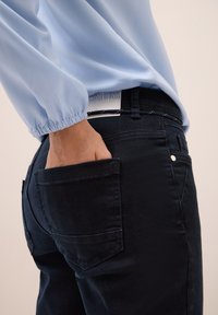 Donkerblauwe spijkerbroek met een slim fit, voorzien van achterzakken en een verborgen knoopsluiting. Het materiaal heeft een gladde textuur met subtiele stiksels.