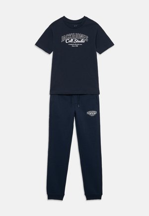 Tyrkysově modré bavlněné tričko s bílým potiskem loga, spárované s odpovídajícími tepláky s elastickým pasem a manžetami na nohavicích.