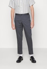 Šedé zúžené kalhoty s hladkým povrchem, v kombinaci s černými botami a bílými ponožkami. Páskovaná košile s krátkým rukávem, knoflíky a kapsou.