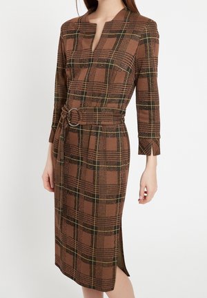 Brązowa sukienka midi w kratę z rękawami do łokcia, w talii pasek z srebrną klamrą i bocznym rozcięciem z przodu.