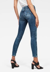 Strakke jeans in donkerblauwe denim met een vervaagde textuur, met een hoge taille, achterzakken en zijnaadjes, gecombineerd met zwarte hoge hakken.