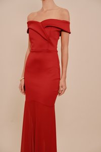 Nő, aki testhez simuló, váll nélküli piros estélyi ruhát visel, amelynek bővülő szegélye van, valamint arany karkötőt a bal csuklóján.