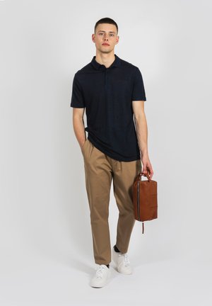 Navy Poloshirt mit kurzen Ärmeln, beige Chinos und weißen Sneakers. Trägt eine braune Ledertasche mit Reißverschluss. Einfaches, lässiges Outfit.