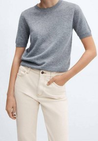 Maglione grigio a maniche corte in morbido tessuto a maglia, con un classico scollo rotondo, abbinato a pantaloni beige con bottone e tasche.