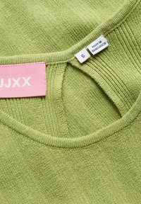 Primo piano dello scollo di un capo in maglia verde chiaro con etichette taglia S e "Made in Bangladesh" e un'etichetta del marchio rosa.