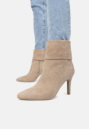 Botas de tobillo de ante beige con punta afilada, parte superior con puño y tacón delgado, usadas con jeans de mezclilla azul claro.