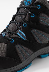 Zwarte en grijze wandelschoen met blauwe accenten, vervaardigd uit mesh en suede materialen, met gestructureerde panelen en robuuste rubberen zolen.