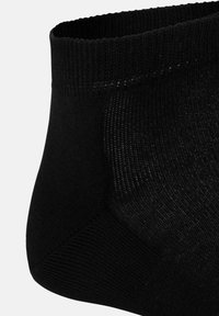 Schwarze Knöchel-Socke mit geripptem Bund, glatter Textur und verstärkter Ferse. Nahaufnahme, die die Nähte und Materialdetails hervorhebt.