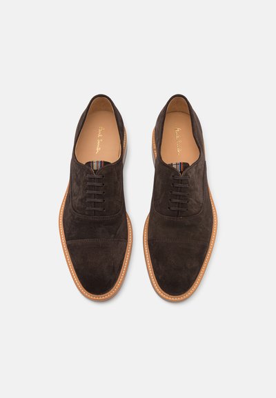 Chaussures en suede marron à lacets avec une semelle en caoutchouc tan contrastante et des coutures, présentant un détail de semelle intérieure rayée.
