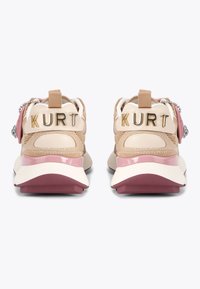 Une paire de baskets beiges et roses vue de l'arrière avec "KURT" en lettres dorées sur les languettes du talon et des charms décoratifs sur les côtés.