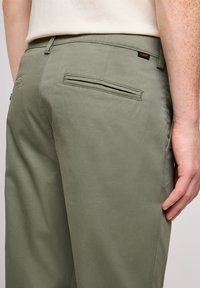 Gröna bomullbyxor med en slät yta, två bakfickor och en liten märkesetikett. Sidofickorna är placerade nära låret.