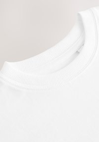 Gros plan d'un T-shirt blanc à col rond montrant les coutures côtelées du col et la texture lisse du tissu en coton.