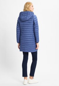 Jasnoniebieska kurtka puchowa z poziomymi szwami, kapturem i kieszeniami po bokach, zestawiona z ciemnymi dżinsami i białymi sneakersami. Gładka, ocieplona tekstura.