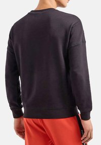 Felpa nera con girocollo, realizzata in tessuto testurizzato. Presenta maniche lunghe e polsini a costine, abbinata a pantaloni sportivi arancioni.