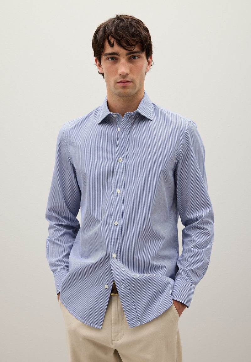 Camisa de botones a rayas azul y blanca, con mangas largas, cuello clásico y dobladillo recto, hecha de una tela ligera.
