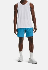 Biała bezrękawnikowa koszulka, niebieskie sportowe szorty, białe sneakersy i białe skarpetki do kostek. Koszulka ma subtelne logo na klatce piersiowej.