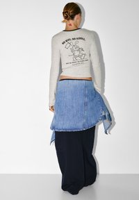 Maglietta grigia a maniche lunghe con dettagli neri, caratterizzata da una grafica di un coniglio in stile cartone animato, abbinata a una gonna di jeans sopra pantaloni scuri.