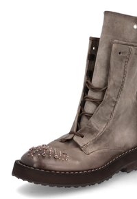 Botte en cuir taupe à lacets avec clous métalliques sur l'avant, semelle épaisse et foncée, et coutures visibles sur les côtés.
