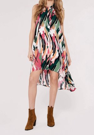 Femme portant une robe sans manches à imprimé abstrait multicolore avec un ourlet asymétrique et des bottines en daim marron.