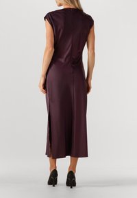 Mauve satin kjole med korte ærmer, ankellang, med lynlås i ryggen og sideslids, glat tekstur og tætsiddende pasform. Sorte højhælede sko synlige.
