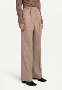 Beige byxhösor med hög midja och vida ben, kombinerade med en brun texturerad tröja och svarta klackboots med spetsig tå.